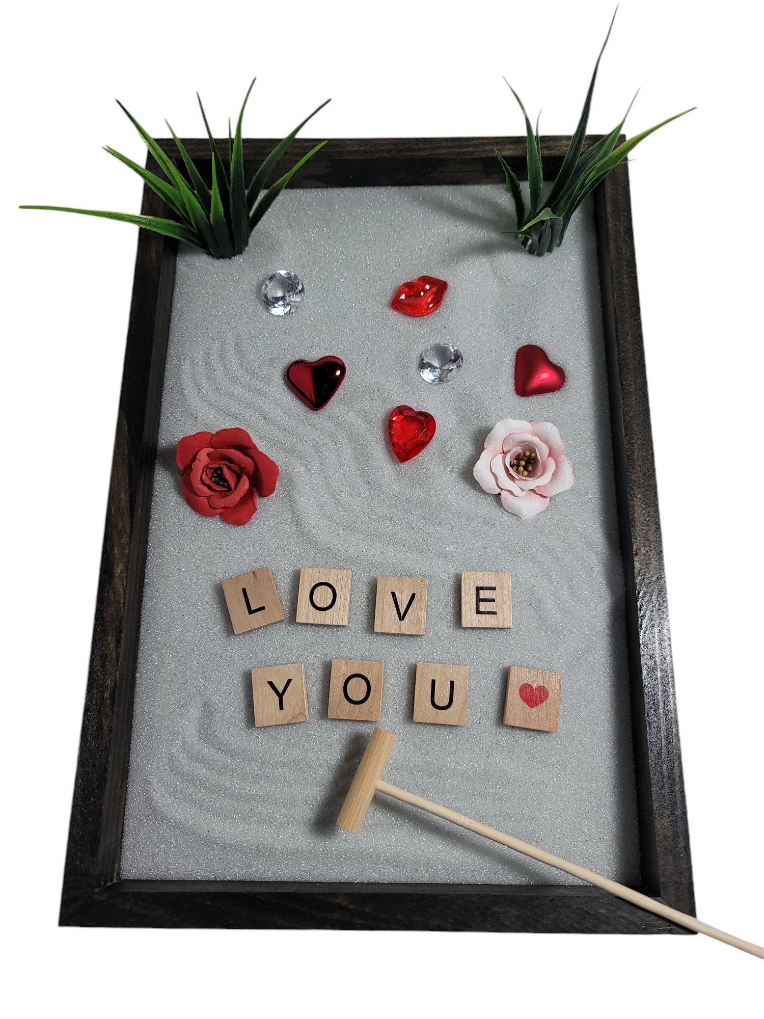 A Love Zen Garden with a bamboo rake, sparkling white sand, red and pink roses, hearts, and the words 'LOVE YOU' spelled out in letter tiles.