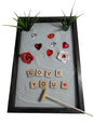 A Love Zen Garden with a bamboo rake, sparkling white sand, red and pink roses, hearts, and the words 'LOVE YOU' spelled out in letter tiles.
