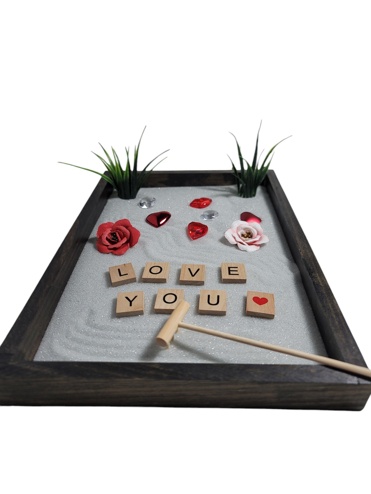 A Love Zen Garden with a bamboo rake, sparkling white sand, red and pink roses, hearts, and the words 'LOVE YOU' spelled out in letter tiles.