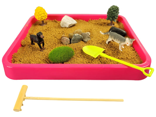 A magenta tray containing play sand with cat and dog figurines, decorative trees, moss rock, polished black stone, white marble stone, and river rocks. 