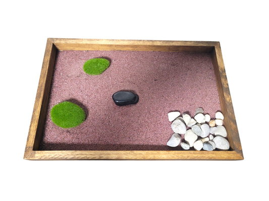 Desktop Zen garden with stones and moss on a purple garnet sand inside a wooden tray.